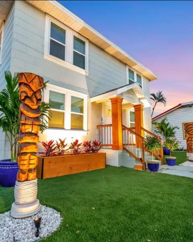 Modern white beach house with orange columns, painted palm tree sculptures, and tropical landscaping at dusk