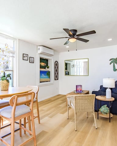 Open-plan living room with dining area, waterfront views through large windows, wood furniture, and dark blue armchair