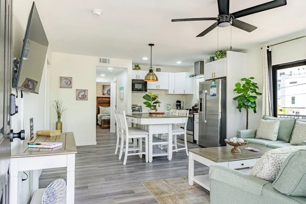 Open-plan kitchen and living room with white cabinetry, stainless steel appliances, dining table, and green upholstered seating.