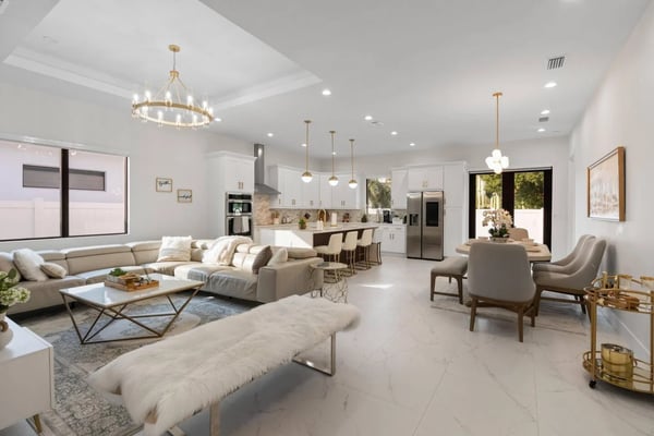 Open-plan living room and kitchen with beige sectional sofa, white cabinetry, stainless steel appliances, and brass pendant lighting