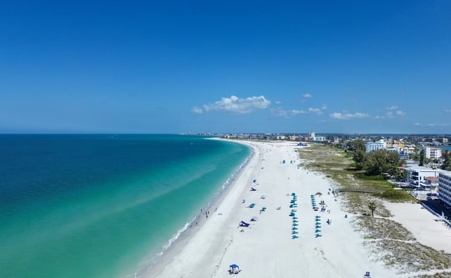 Aerial view of wide sandy beach with turquoise water, blue umbrellas, and beachfront hotels and buildings